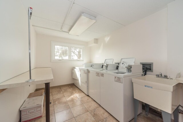 common laundry area with light tile patterned floors, washing machine and dryer, and a sink