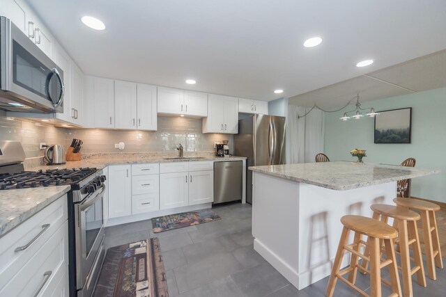 kitchen with a kitchen breakfast bar, white cabinetry, a sink, appliances with stainless steel finishes, and backsplash