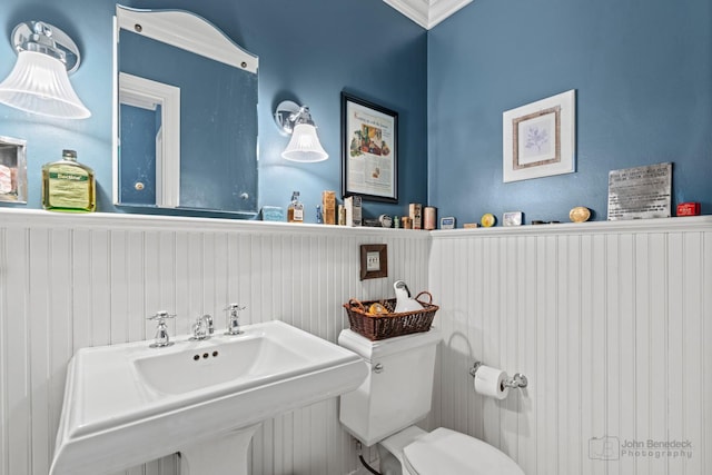 bathroom featuring toilet, crown molding, a wainscoted wall, and a sink
