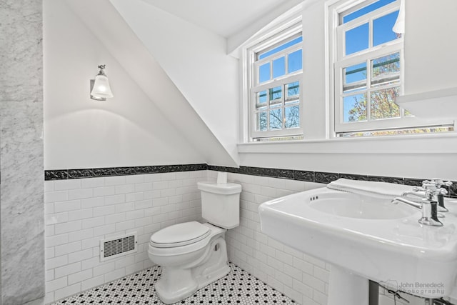 bathroom with tile walls, a sink, toilet, visible vents, and wainscoting