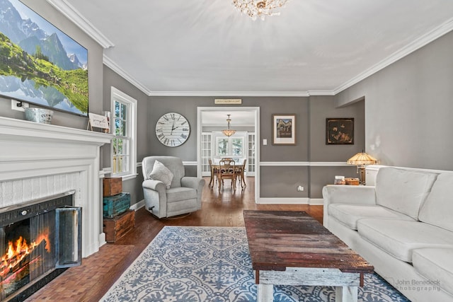 living room with wood finished floors, ornamental molding, a lit fireplace, and a notable chandelier