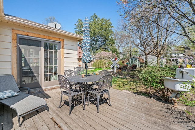 deck featuring a storage unit, outdoor dining space, and an outbuilding