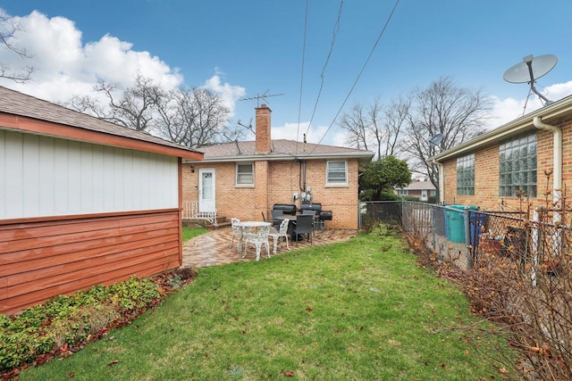rear view of house featuring a chimney, fence, brick siding, a yard, and a patio