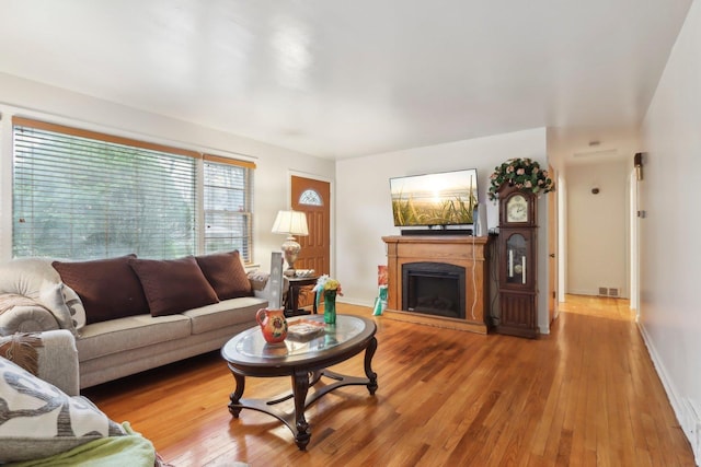 living area featuring visible vents, baseboards, a fireplace with raised hearth, and wood-type flooring