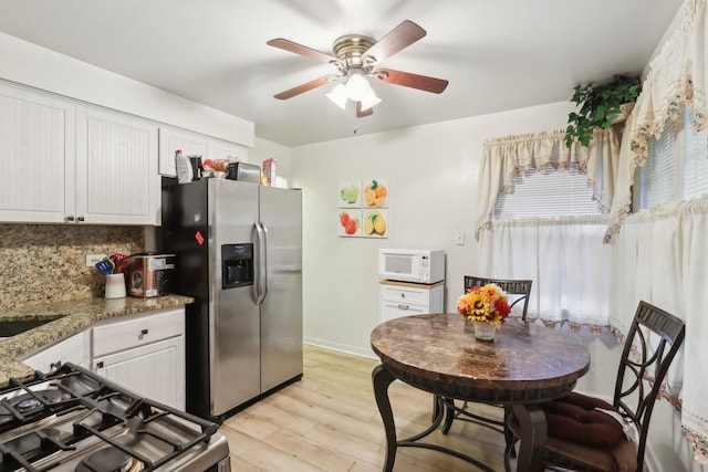 kitchen with light wood finished floors, stainless steel fridge with ice dispenser, range with gas cooktop, a ceiling fan, and white microwave