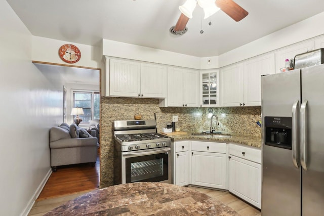 kitchen featuring stainless steel appliances, light wood-style flooring, a sink, backsplash, and a ceiling fan