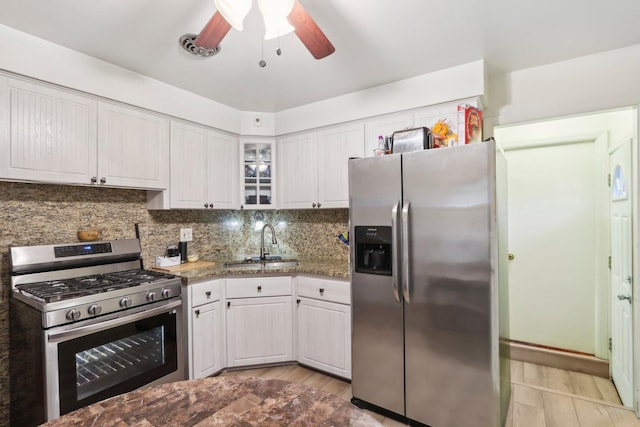 kitchen featuring white cabinets, stainless steel appliances, a sink, decorative backsplash, and ceiling fan