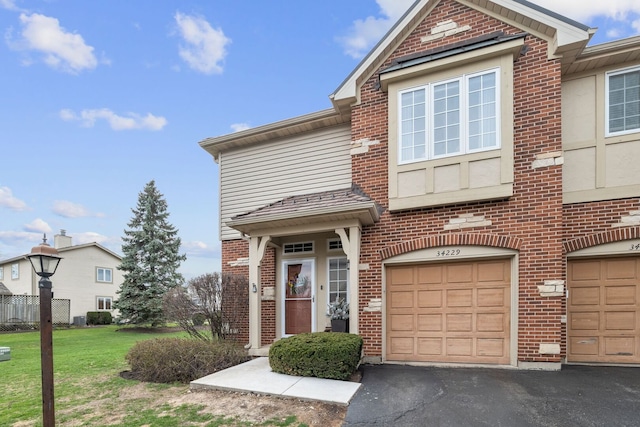 townhome / multi-family property with brick siding, a front yard, driveway, and a garage