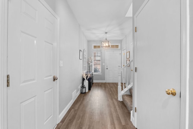 entryway with wood finished floors, stairs, an inviting chandelier, baseboards, and visible vents