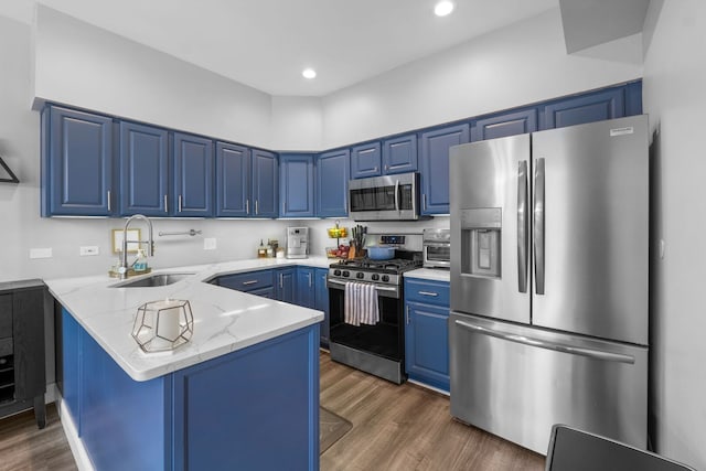 kitchen with blue cabinets, a peninsula, a sink, light stone counters, and appliances with stainless steel finishes