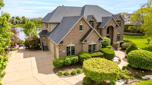 view of front of property featuring brick siding, driveway, a water view, fence, and roof with shingles