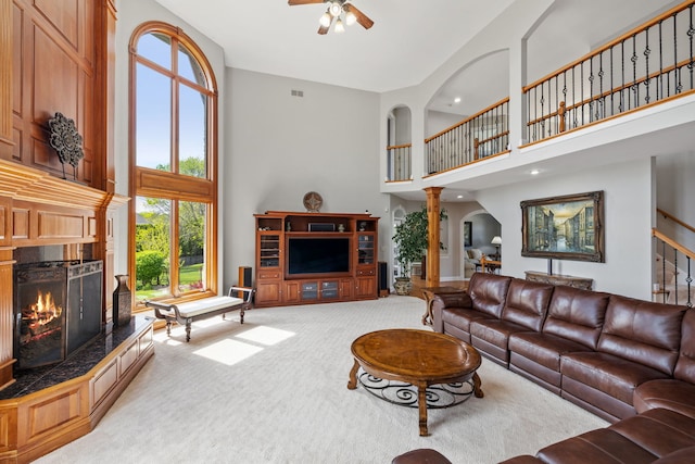 living room with a towering ceiling, carpet floors, a warm lit fireplace, ceiling fan, and arched walkways