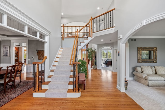 stairway featuring arched walkways, wood finished floors, a towering ceiling, recessed lighting, and baseboards