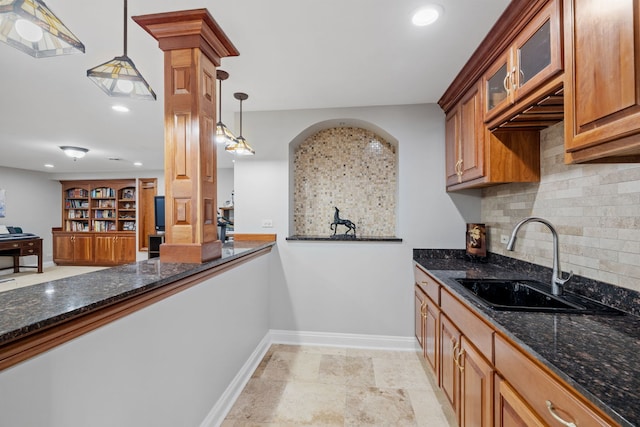 kitchen with a sink, baseboards, backsplash, dark stone countertops, and pendant lighting