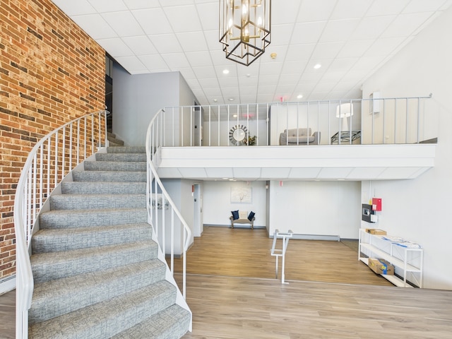 stairway featuring recessed lighting, an inviting chandelier, brick wall, a towering ceiling, and wood finished floors