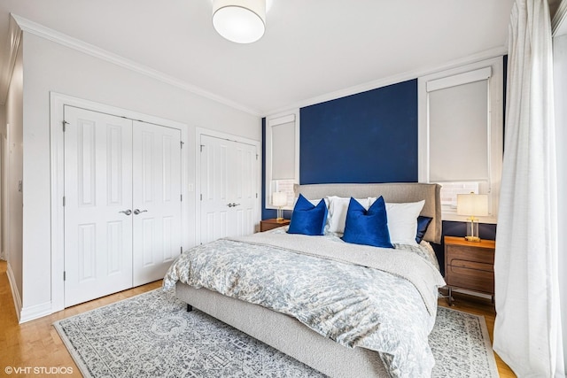 bedroom featuring multiple closets, light wood-type flooring, ornamental molding, and baseboards