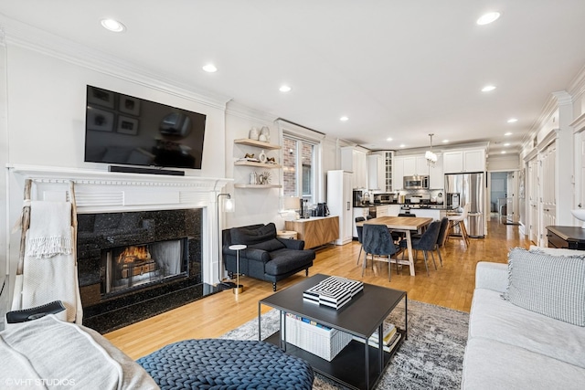 living room featuring ornamental molding, a high end fireplace, light wood-style flooring, and recessed lighting