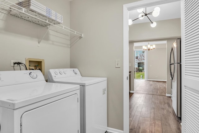 clothes washing area with washer and clothes dryer, baseboards, a notable chandelier, laundry area, and wood-type flooring