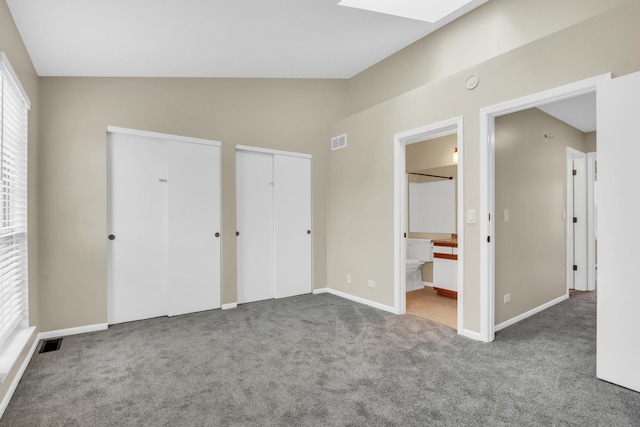 unfurnished bedroom featuring visible vents, baseboards, vaulted ceiling with skylight, two closets, and carpet flooring