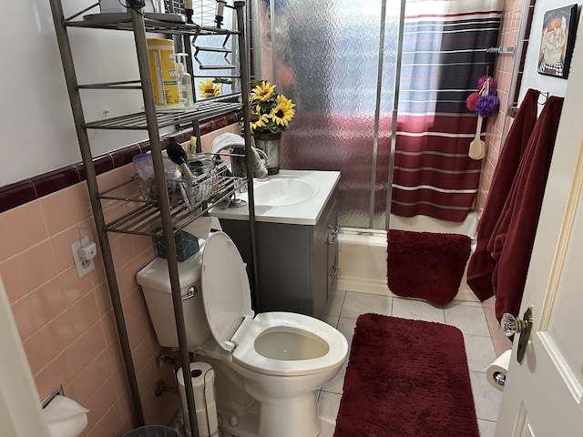 bathroom with tile patterned flooring, enclosed tub / shower combo, toilet, vanity, and tile walls