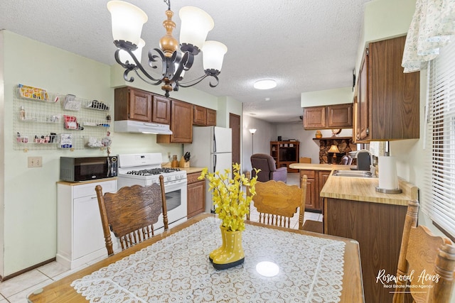 kitchen with under cabinet range hood, an inviting chandelier, a sink, white appliances, and a textured ceiling