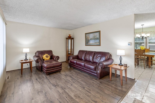 living area featuring wood finished floors, a textured ceiling, a notable chandelier, and visible vents