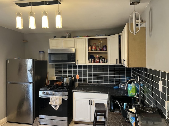 kitchen with dark stone countertops, a sink, decorative backsplash, stainless steel range with gas stovetop, and freestanding refrigerator