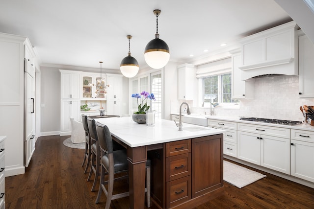 kitchen with a kitchen breakfast bar, a center island with sink, white cabinetry, a sink, and stainless steel gas stovetop