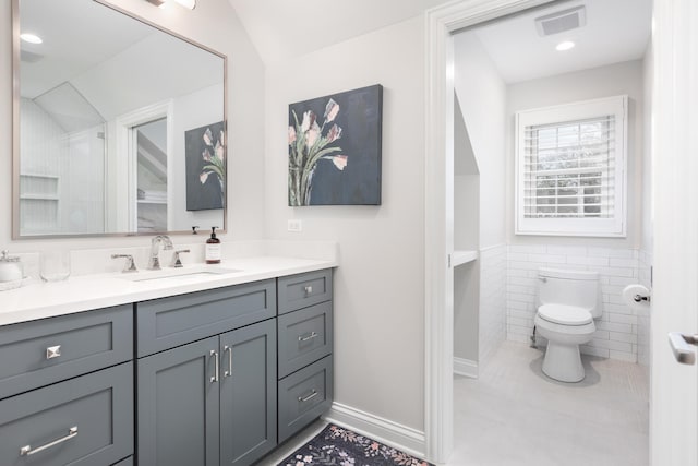 bathroom with visible vents, vanity, toilet, tile walls, and tile patterned floors