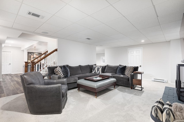 living area with visible vents, baseboards, a drop ceiling, and stairway