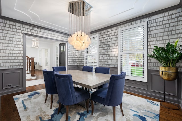 dining area with an inviting chandelier, ornamental molding, wood finished floors, wallpapered walls, and a wainscoted wall