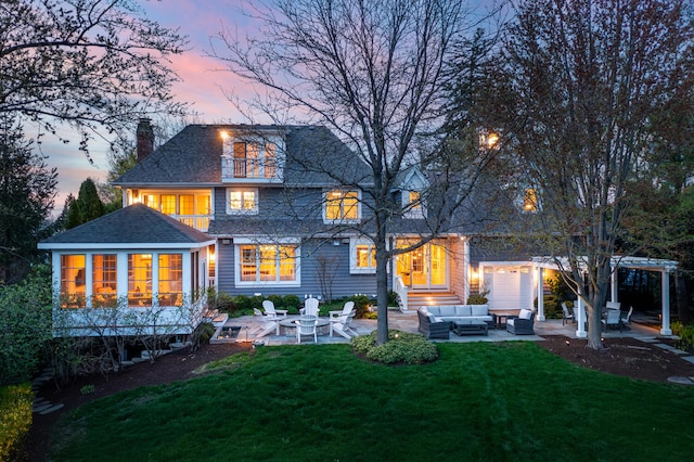 back of house at dusk featuring a patio, a chimney, an outdoor living space, a shingled roof, and a yard
