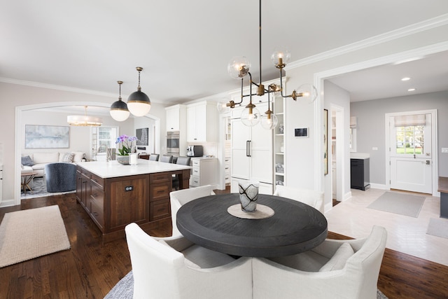 dining area featuring dark wood-style flooring, arched walkways, a chandelier, and ornamental molding