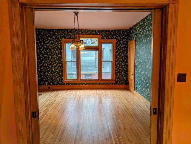 907 W Church St, Champaign, IL 61821 - spare room with wallpapered walls, baseboards, wood finished floors, and a chandelier