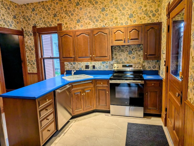 907 W Church St, Champaign, IL 61821 - kitchen featuring wallpapered walls, appliances with stainless steel finishes, a sink, wainscoting, and brown cabinetry