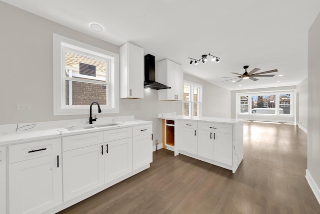 kitchen with light stone counters, wood finished floors, a sink, ceiling fan, and wall chimney exhaust hood