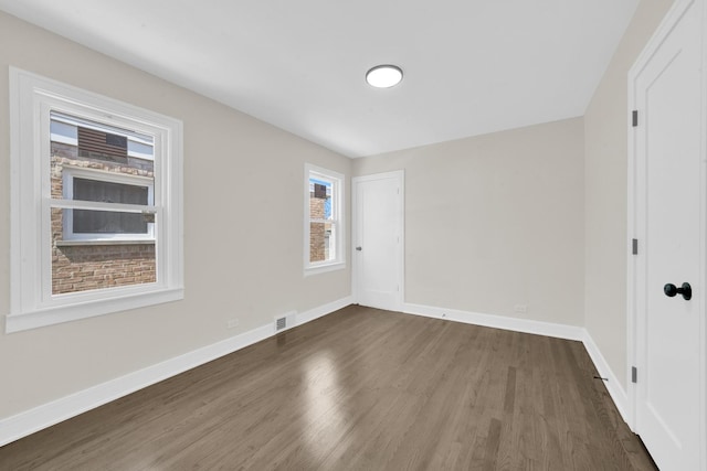 empty room featuring visible vents, baseboards, and dark wood-style flooring
