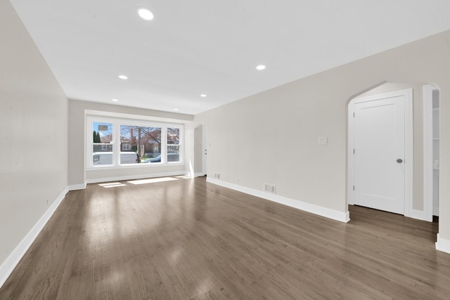 unfurnished living room with wood finished floors, arched walkways, baseboards, visible vents, and recessed lighting