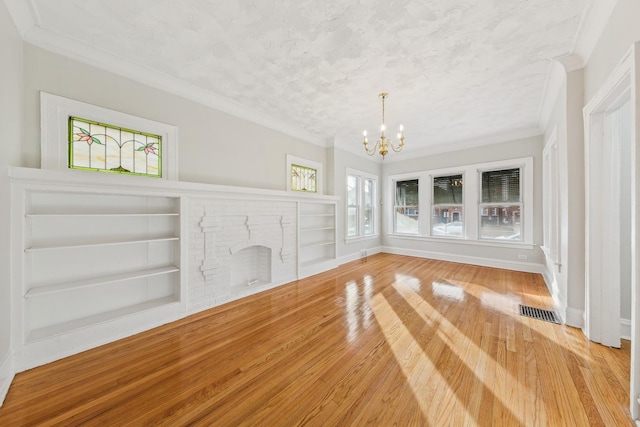 unfurnished living room with built in shelves, crown molding, wood finished floors, and a chandelier