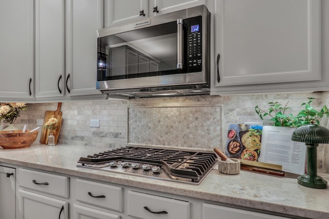 kitchen with white cabinets, backsplash, light stone counters, and stainless steel appliances