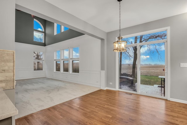 unfurnished dining area with a decorative wall, wood finished floors, wainscoting, an inviting chandelier, and visible vents