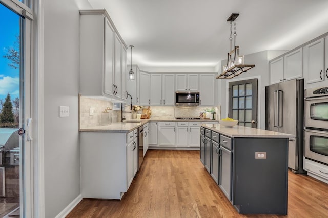 kitchen featuring light wood-style flooring, backsplash, gray cabinetry, decorative light fixtures, and appliances with stainless steel finishes
