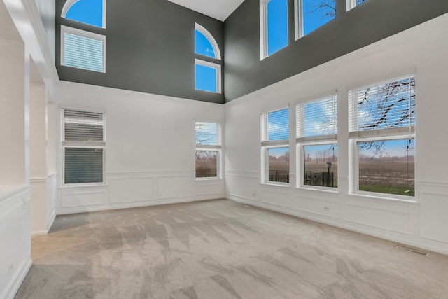 carpeted spare room featuring visible vents, a wainscoted wall, a high ceiling, and a decorative wall