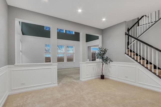 unfurnished living room with light colored carpet, a decorative wall, and stairs