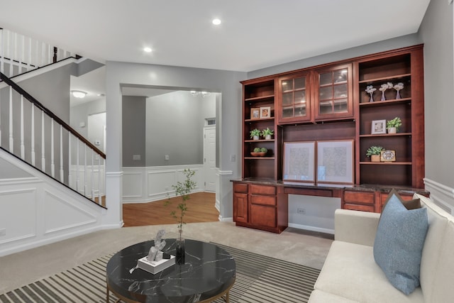living room with a decorative wall, stairs, wainscoting, light colored carpet, and recessed lighting