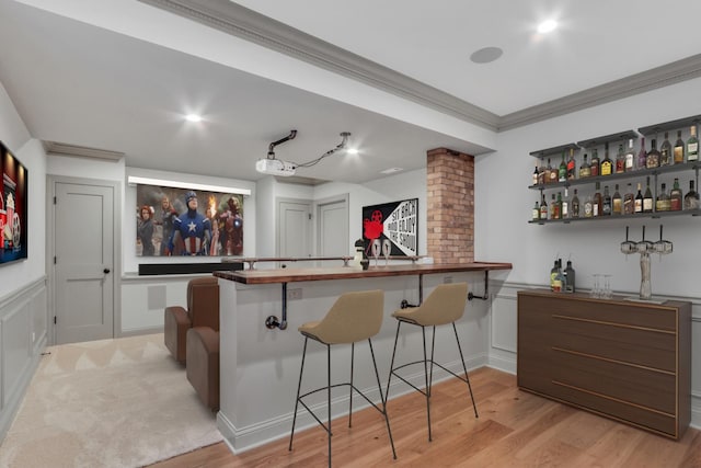 bar featuring a decorative wall, a bar, a wainscoted wall, light wood-style flooring, and ornamental molding