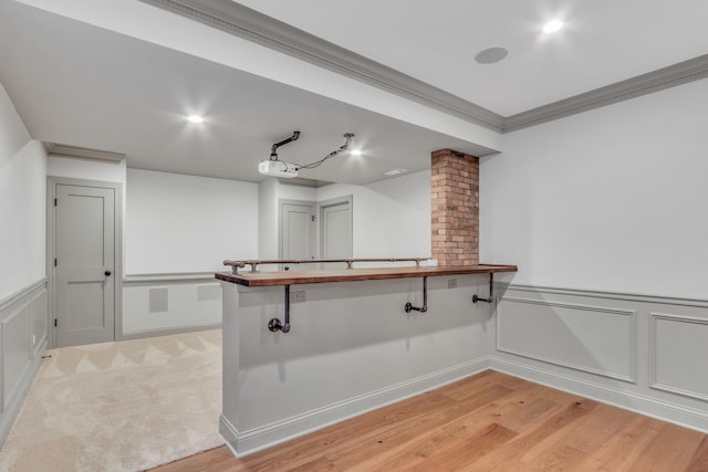 bar with a decorative wall, a wainscoted wall, light wood finished floors, ornamental molding, and decorative columns