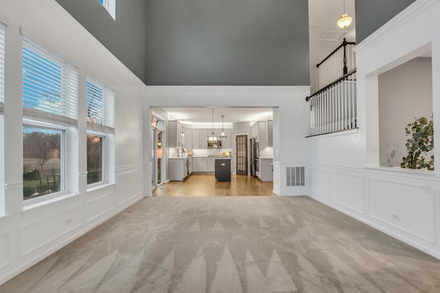 unfurnished living room featuring a decorative wall, a towering ceiling, light colored carpet, and visible vents