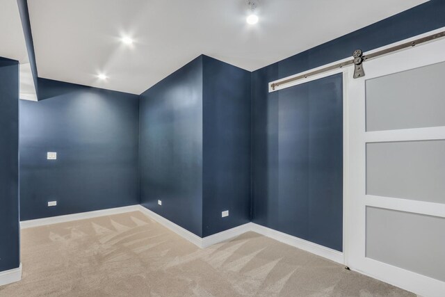 empty room with a barn door, carpet floors, and baseboards