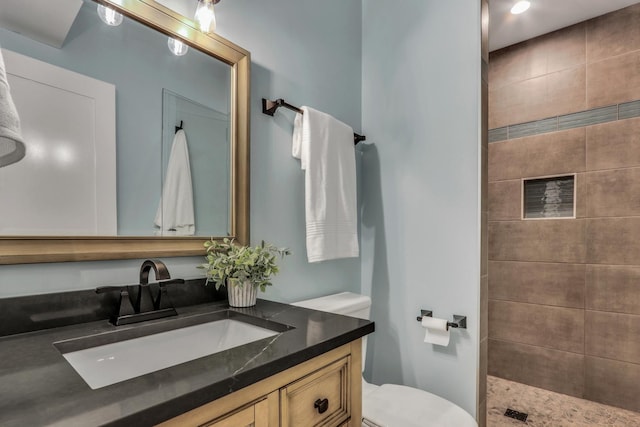 full bathroom featuring a tile shower, toilet, and vanity